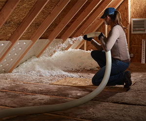 Female worker installing blown-in insulation in an attic.