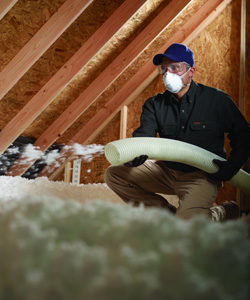 Worker installing blown-in insulation in an attic.