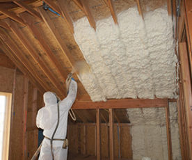 Worker wearing protective gear installing spray foam insulation on a ceiling.