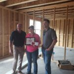 Dani Krug stands between teammates at a job site proudly showing her CEE award