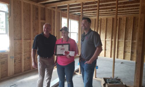 Dani Krug stands between teammates at a job site proudly showing her CEE award