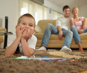 Happy child playing on a carpeted floor with his parents on the couch behind him.