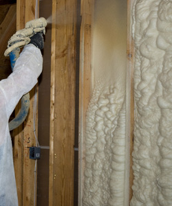 Worker installing spray foam insulation in an interior wall.