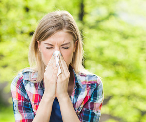 Woman sneezing outside, using a tissue.