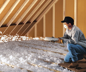 Worker installing blown-in insulation in an attic.