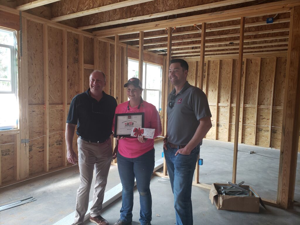 Dani Krug stands between teammates at a job site proudly showing her CEE award