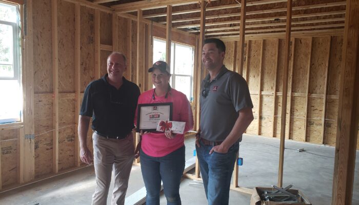 Dani Krug stands between teammates at a job site proudly showing her CEE award